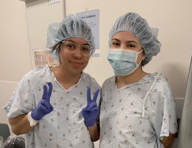 Two sisters in hospital gowns and hair coverings prepare for surgery.