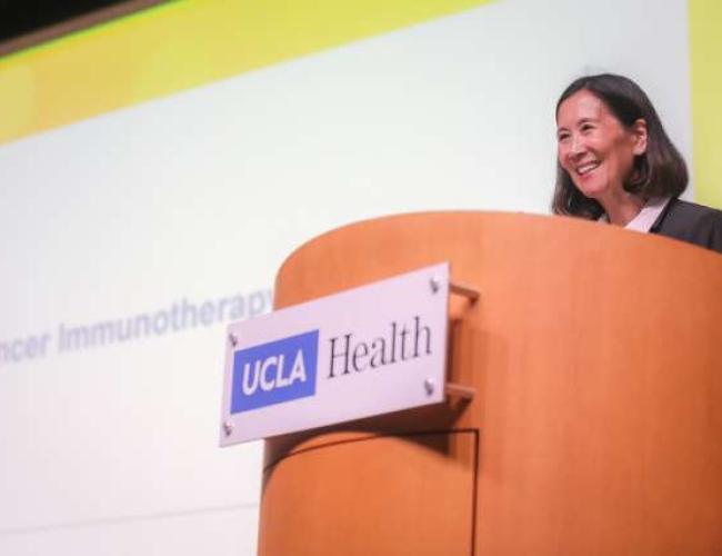 Dr. Linda Liau smiling behind a podium with a UCLA Health plaque on it.