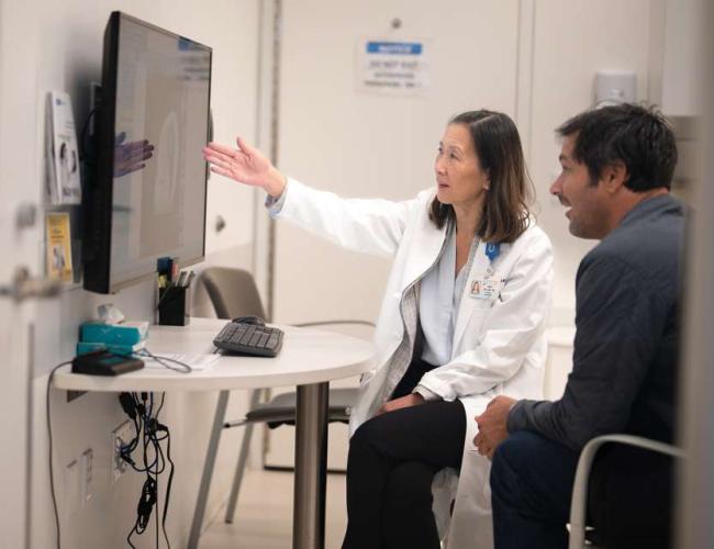 Dr. Linda Liau points to a screen while sitting with a patient