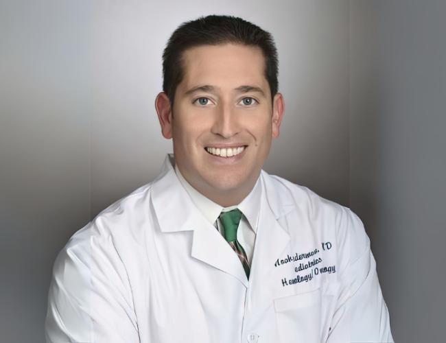 A doctor in a whitecoat smiles for a headshot.