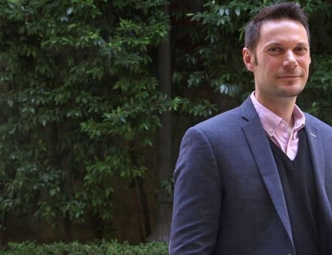 Patrick Allard stands smiling before deep green trees.