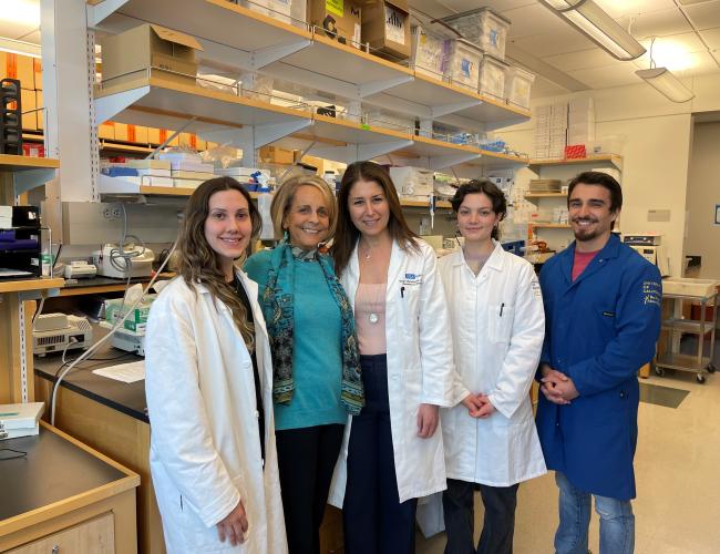 A group of researchers stand smiling in a lab with a donor and patient advocate. 