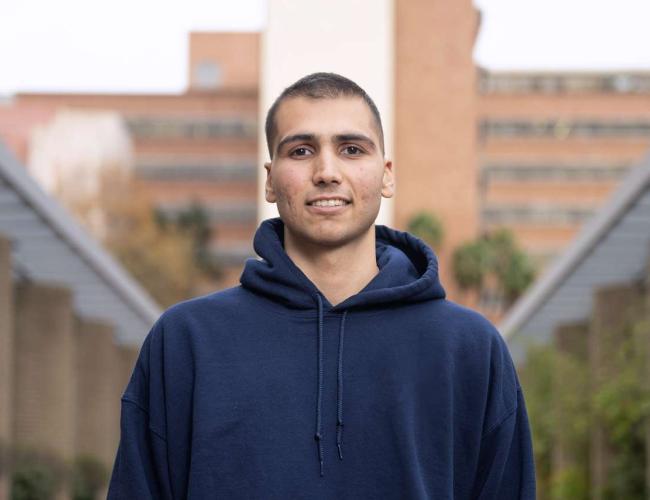 Sina Sinbari wears a dark blue hoodie and smiles into the camera. 