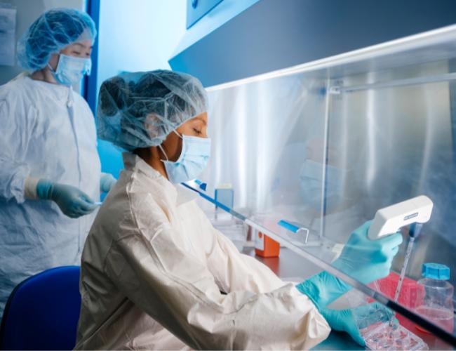 Two scientists wearing PPE work at a station in a UCLA cell therapy lab.