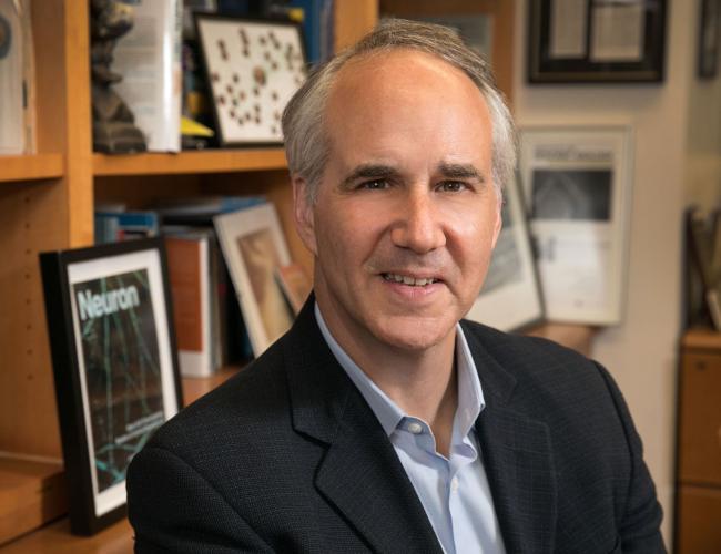 A close-up photograph of researcher Daniel Geschwind smiling in his office before a bookshelf.