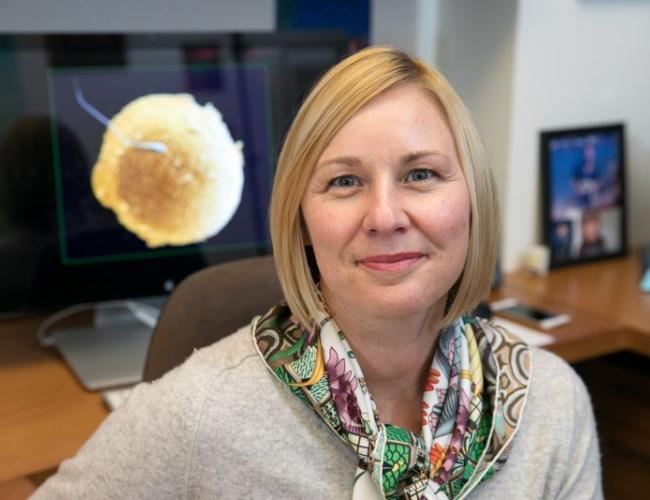 Researcher Amander Clark smiles at her desk, wearing a brightly colored scarf.