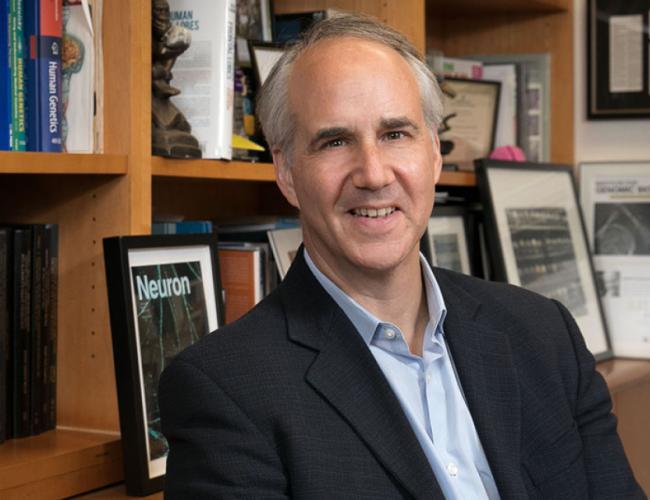 Researcher Daniel Geschwind smiles in his office before a bookshelf.