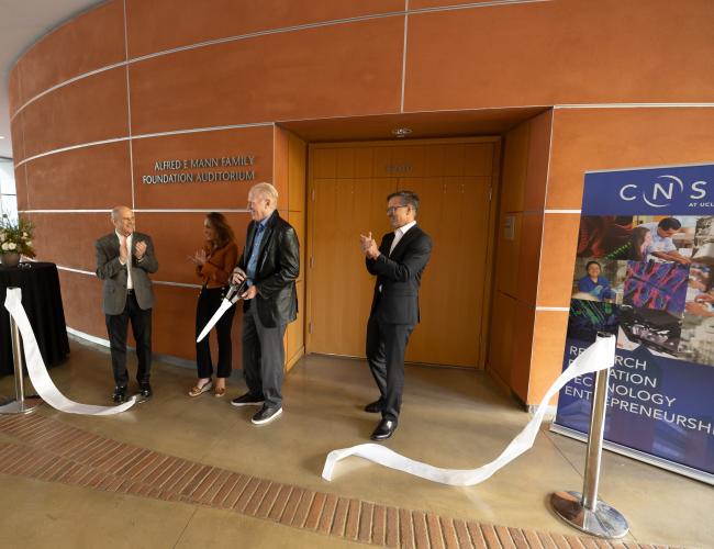 A group of people gather around a cut ribbon in a building 