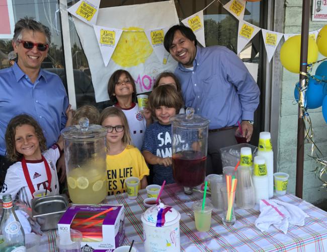 Children take a photo in front of lemonade stand with UCLA researcher.