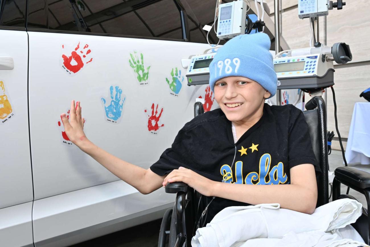 cancer patient Jake Brandes sitting in a wheelchair smiling putting his handprint on a white car during the Hyundai Hope on Wheels handprint ceremony