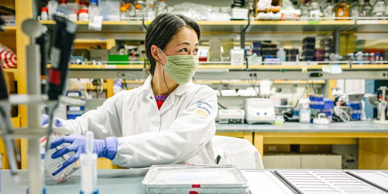 A UCLA researcher with smiling eyes looks out of frame while working in a laboratory. 