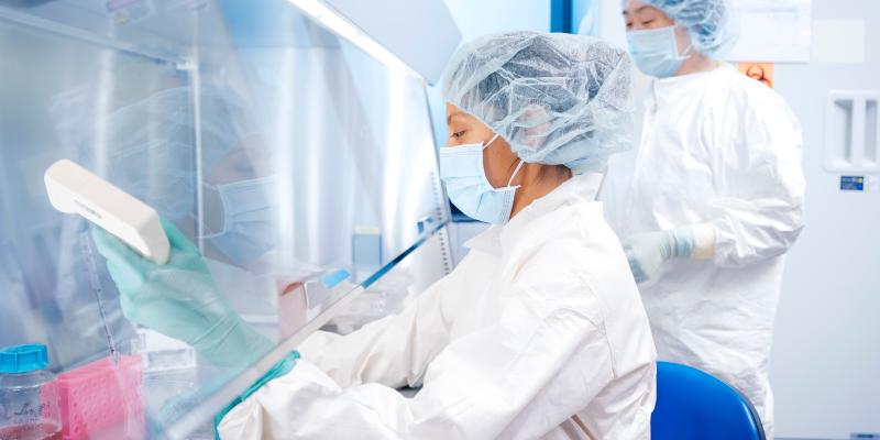 Two female scientists work at a hood in a GMP facility in UCLA.
