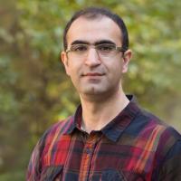 A man smiles at the camera while standing outdoors.