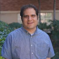 UCLA scientist Jason Ernst smiles for a photograph. He wears a blue collared short-sleeve shirt and stands outdoors on the UCLA campus.