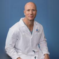 Jeffrey Veale smiles for a photograph. He dons a white labcoat.