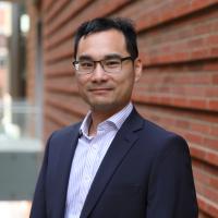 Researcher Neil Lin smiles in a headshot taken outside. 
