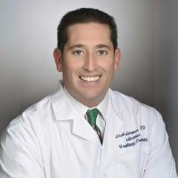 A doctor in a whitecoat smiles for a headshot.