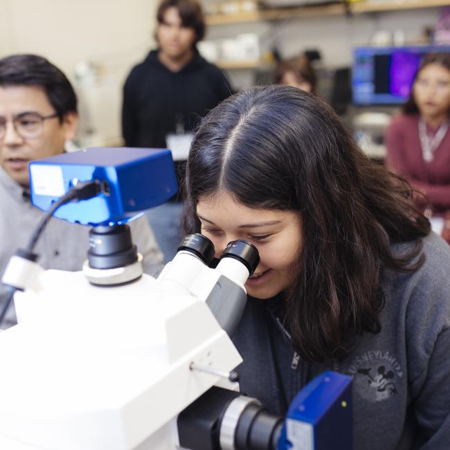 female high school student wearing a grey disneyland hoodie looks through a microscope