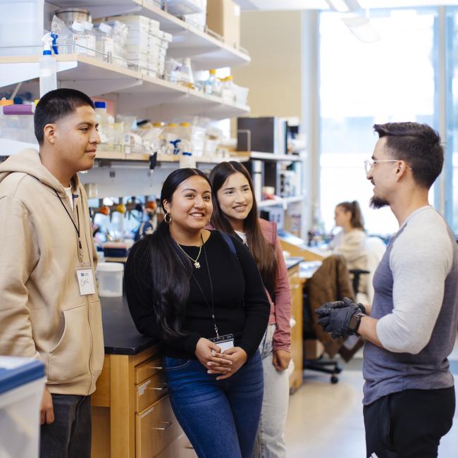 one male high school student and two female high school students are in a UCLA lab with a male scientist leading the tour