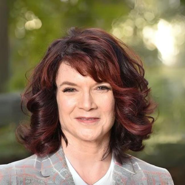 A woman smiles into the camera while standing outdoors.