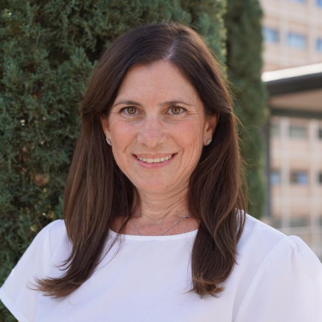 Headshot of BSCRC trainee Aya Barzelay, an individual with long dark hair wearing a white top, smiling outdoors.