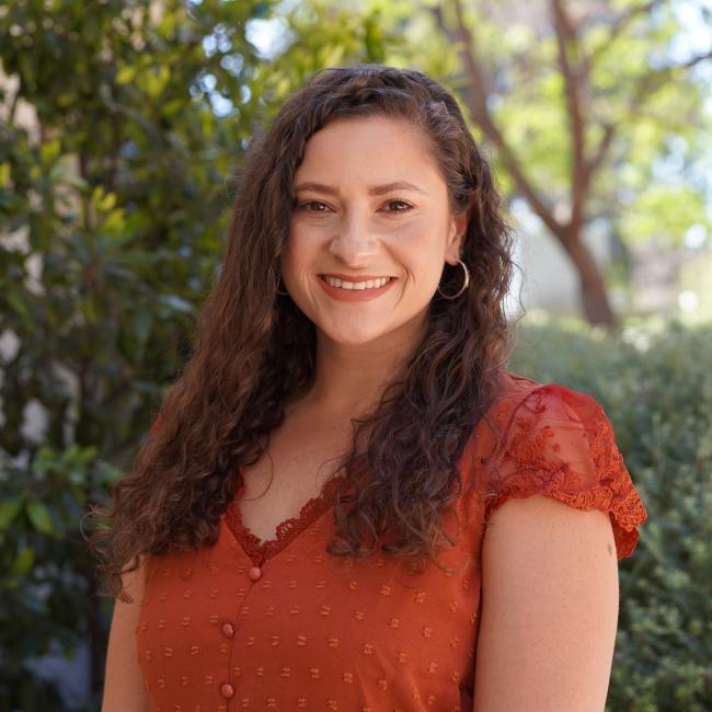 Female Admin with long brown hair wearing an orange shirt. 