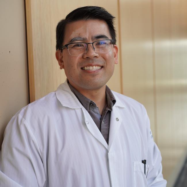 Male researcher with short dark hair wearing a white lab coat.