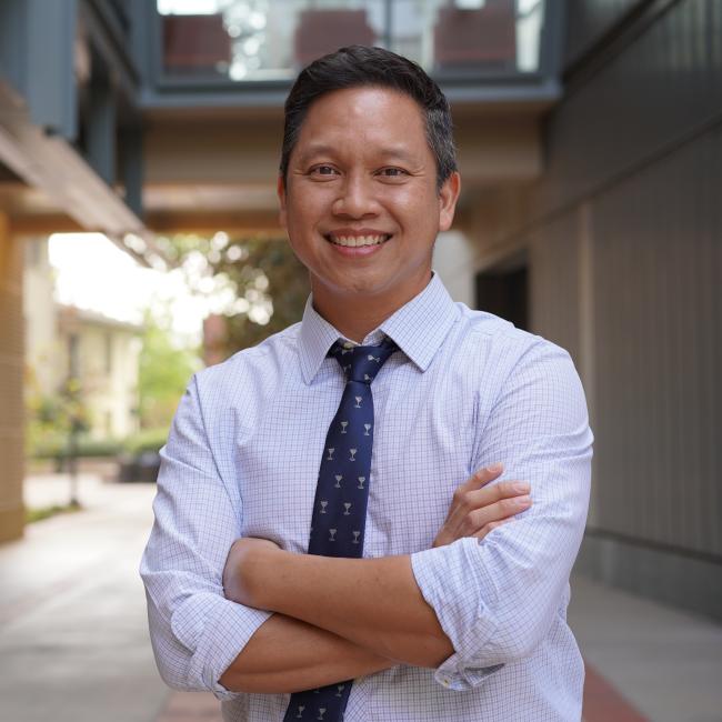 Male researcher with short dark hair wearing a white shirt and dark tie.