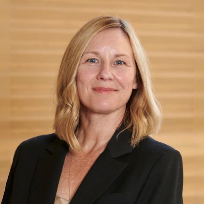 Amander Clark wears a dark blazer and smiles into the camera. 