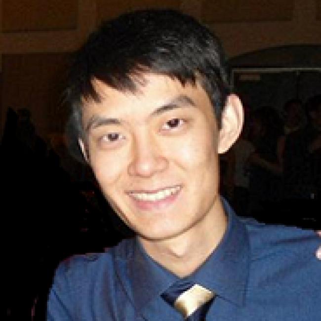 Headshot of Andrew King, a person with short dark hair, smiling in an indoor setting, wearing a dark blue shirt.
