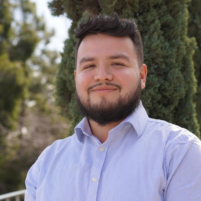 headshot of trainee Carlos Galvan who is wearing a light blue collared shirt and standing in front of trees