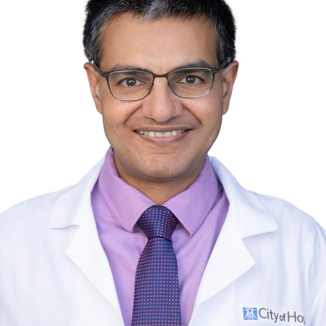 Headshot of Chintan Parekh, a person with short dark hair and glasses, smiling against a white background, wearing a white City of Hope lab coat, lavender shirt, and blue patterned tie.