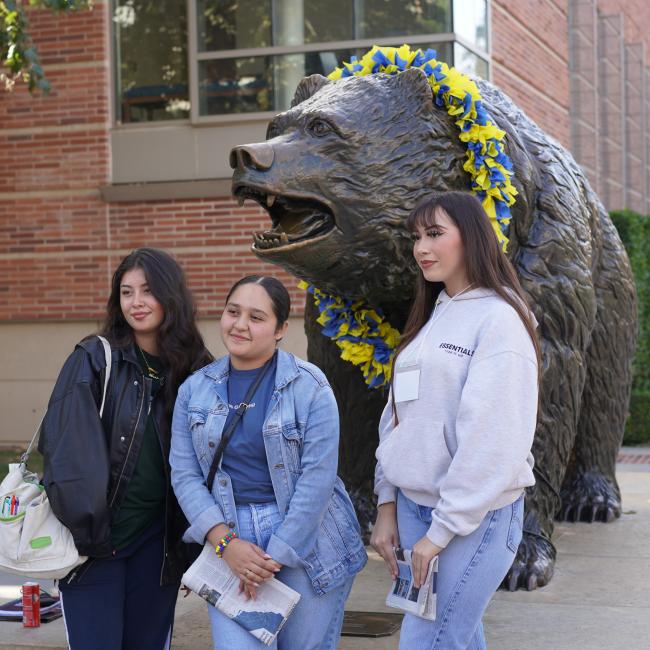 three female high school students pose for a photo in front of the bruin bear statue on the ucla campus