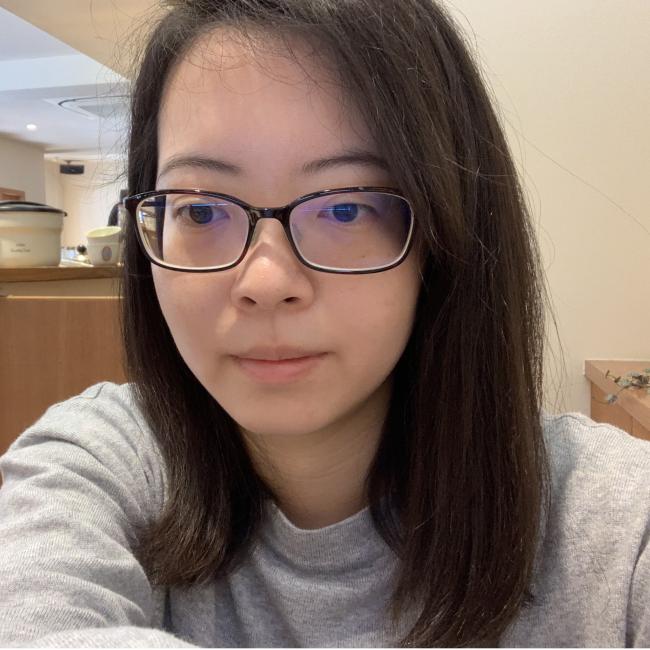 Headshot of Fei-man Hsu, a person with long dark hair and rectangular glasses, wearing a gray sweatshirt, photographed indoors.