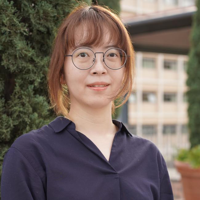 Headshot of Fei-Man Hsu, a woman with brown hair and round glasses wearing a dark navy blouse, smiling outdoors.