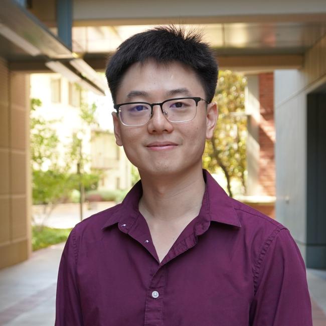Male Scientist with short dark hair wearing a purple shirt.