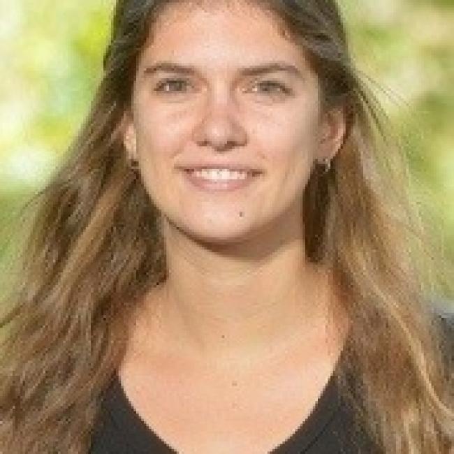 Headshot of Grace Hancock, a woman with long brown hair, smiling outdoors against a blurred green background.
