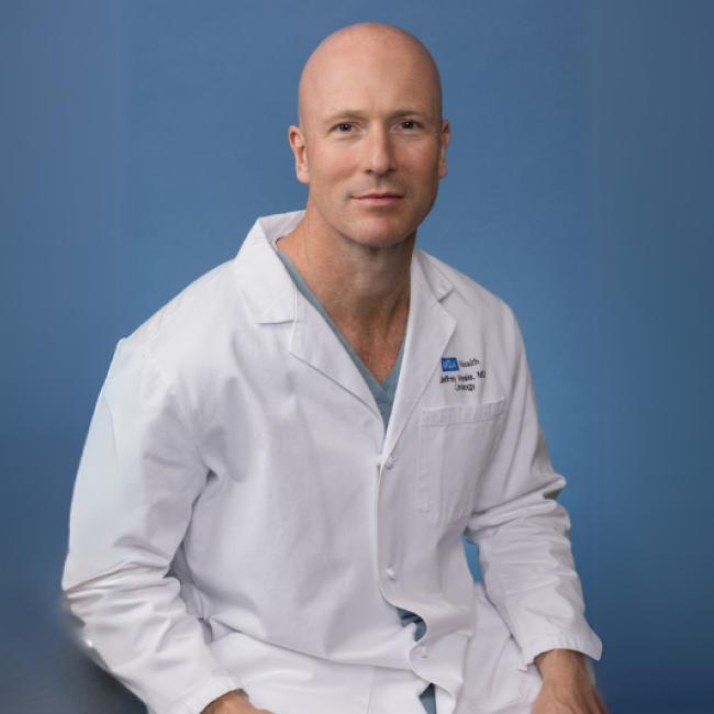 Jeffrey Veale smiles for a photograph. He dons a white labcoat.