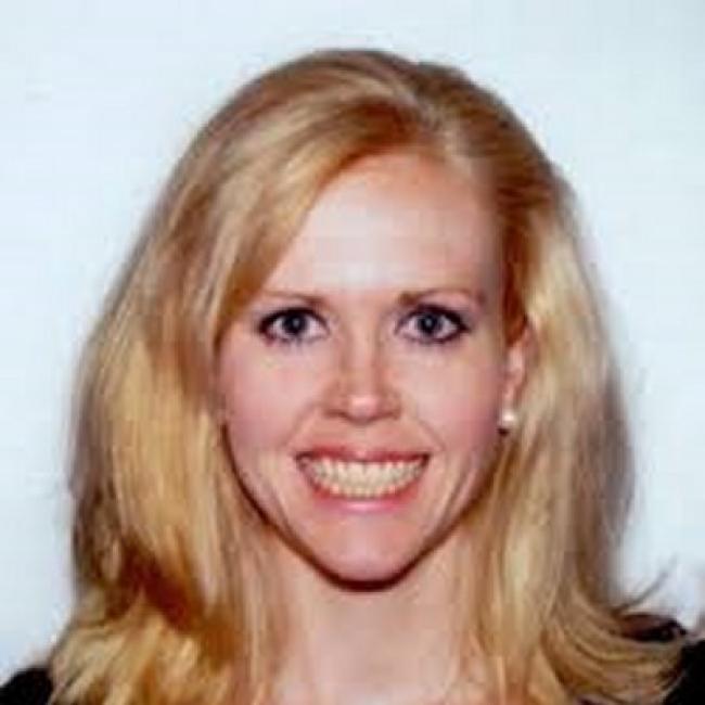Headshot of Jennifer Kasten, a person with long blonde hair and blue eyes, smiling against a dark background.