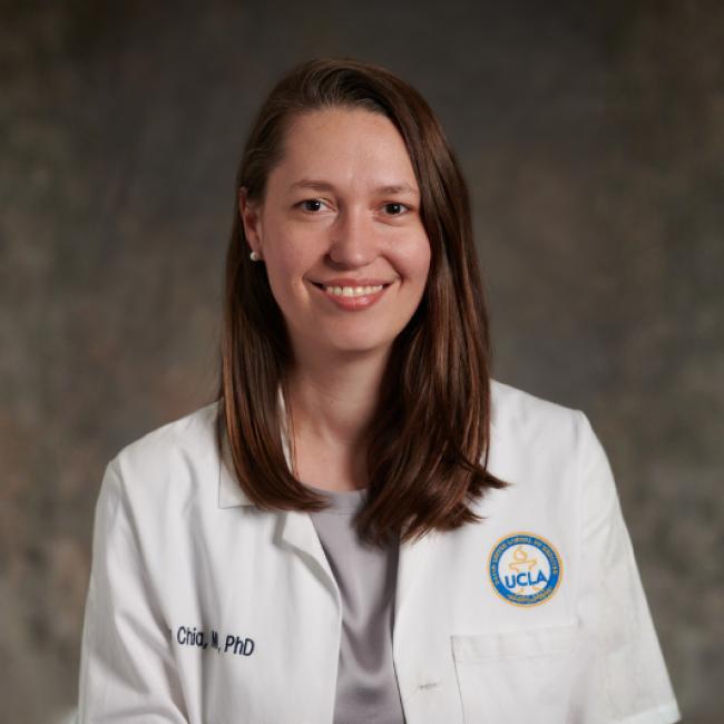 UCLA physician-scientist Jennifer Chia smiles for a headshot in a white labcoat in front of a muted brown background.