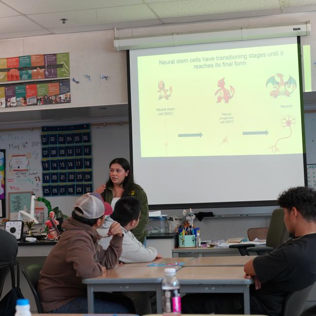 trainee jessenya mil presenting to high school students in front of a classroom with a slide on pokemon evolution in the background