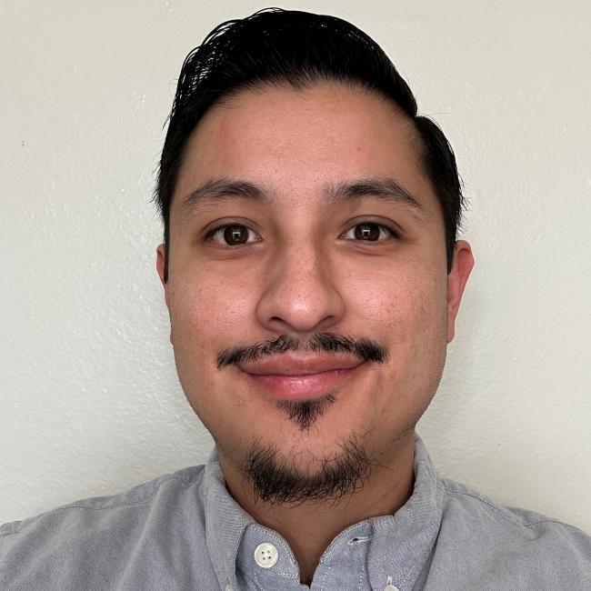 A headshot of Johnny Diaz, who is pictured smiling and wearing a pale blue button-up shirt. He has dark, short hair. 