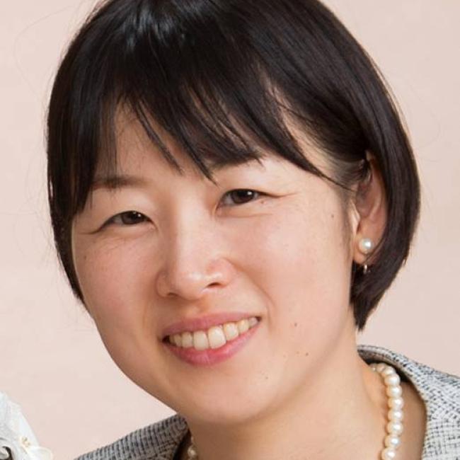 Headshot of Momoko Watanabe, a person with short dark hair, smiling against a light beige background, wearing a gray blazer and pearl necklace.