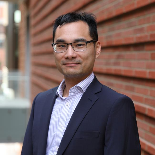 Researcher Neil Lin smiles in a headshot taken outside. 