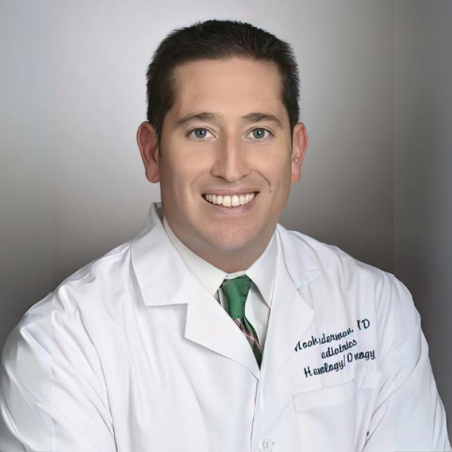 A doctor in a whitecoat smiles for a headshot.