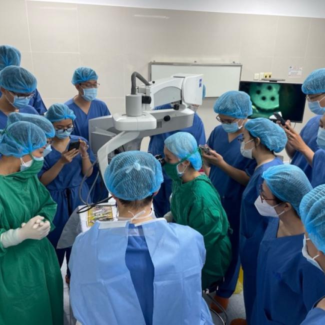 A group of ophthalmologists huddles together for a skill transfer session with Dr. Anthony Aldave.