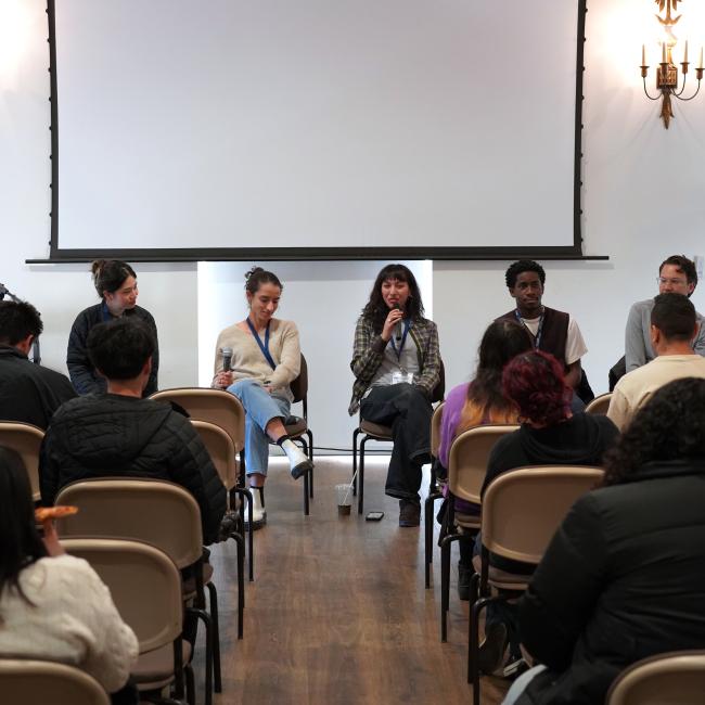 five panelists sitting down in front of a room in front of seated high school students