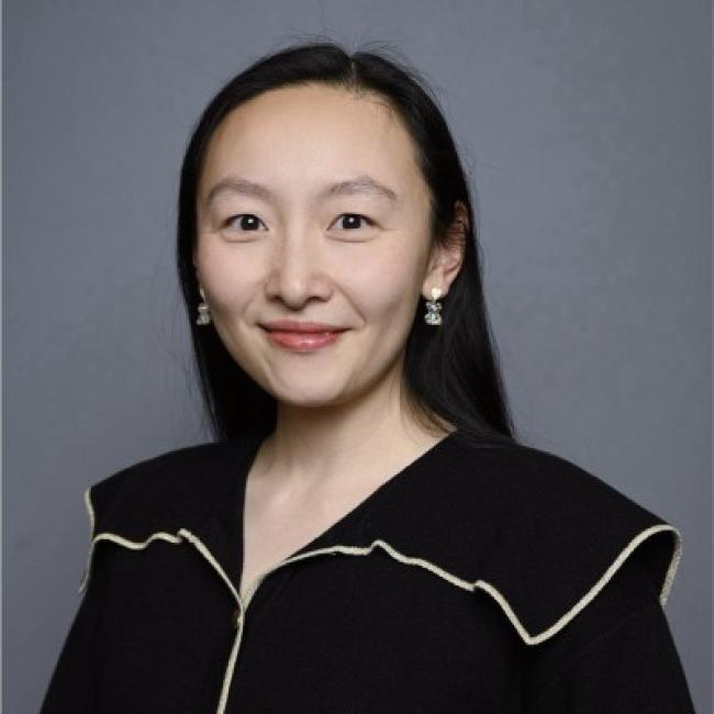 Headshot of Wenyuan (Wen) Wang, a person with long dark hair and decorative earrings, smiling against a gray background, wearing a black top with cream trim.