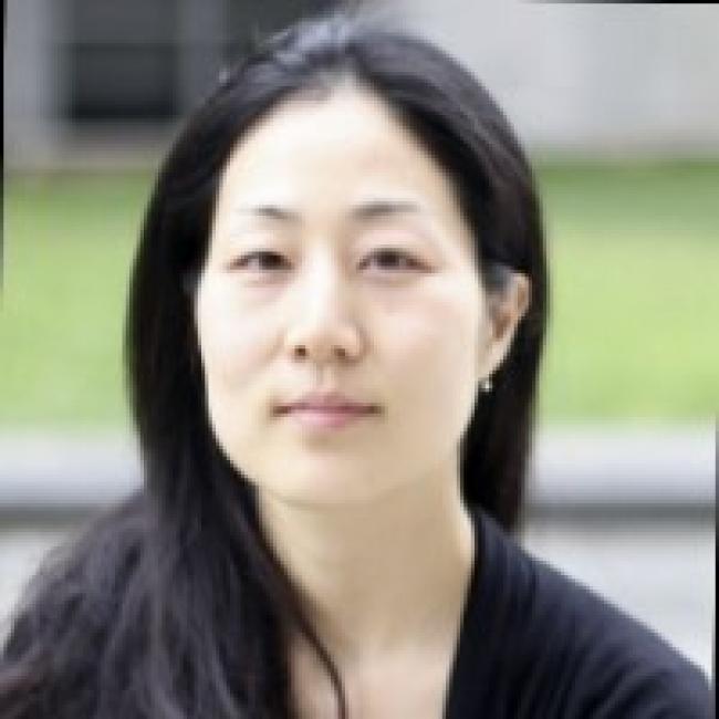 Headshot of Kay (Kyu-hyeon) Yeom, a person with short dark hair, against a blurred outdoor background, wearing a dark top.