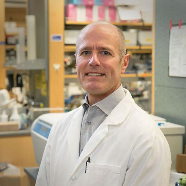 Headshot of S. Thomas Carmichael in a lab coat smiles in a UCLA lab